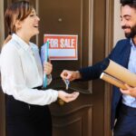 a real estate agent is handling the keys to the owner after it got sold